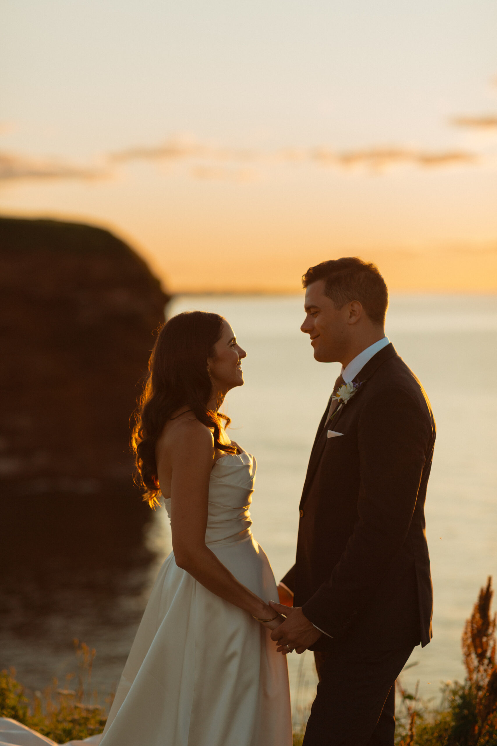 bride and groom smiling holding hands looking at each other standing on cliff