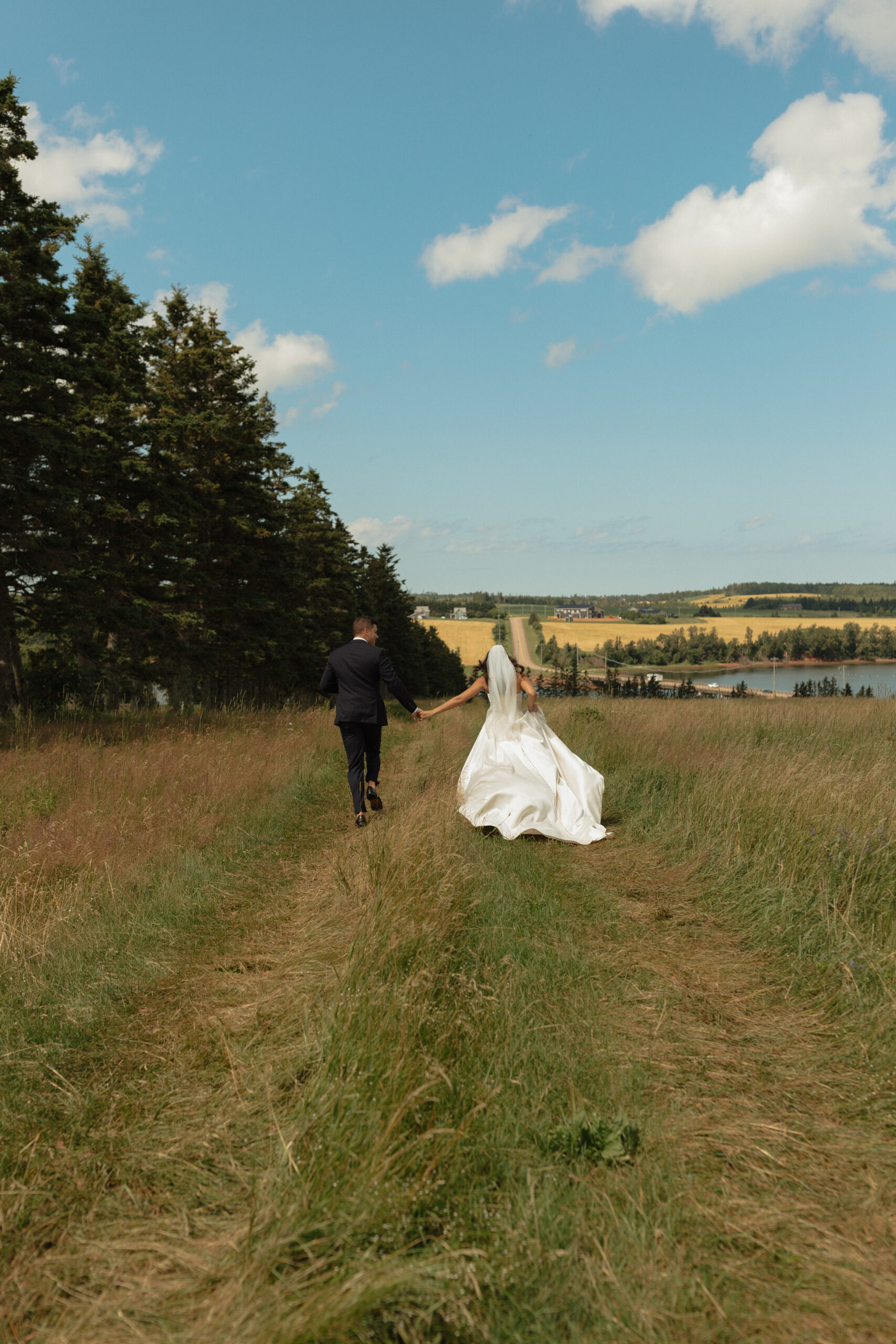 bride and groom running through field, wedding dress flowing in the wind