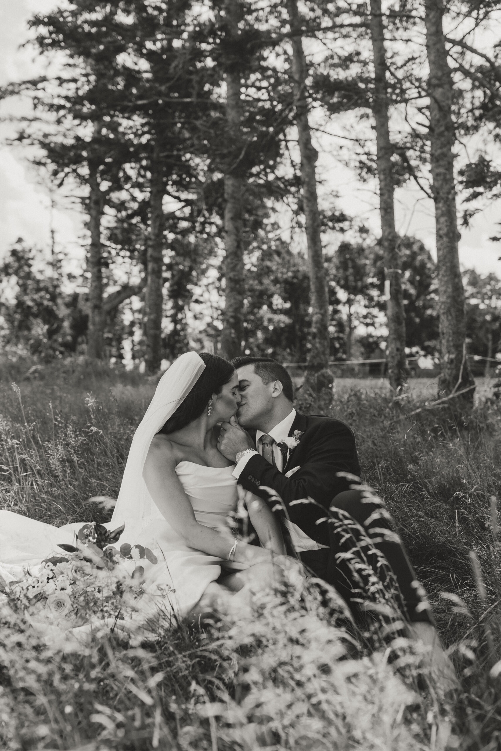 bride and groom kissing while sitting in a field