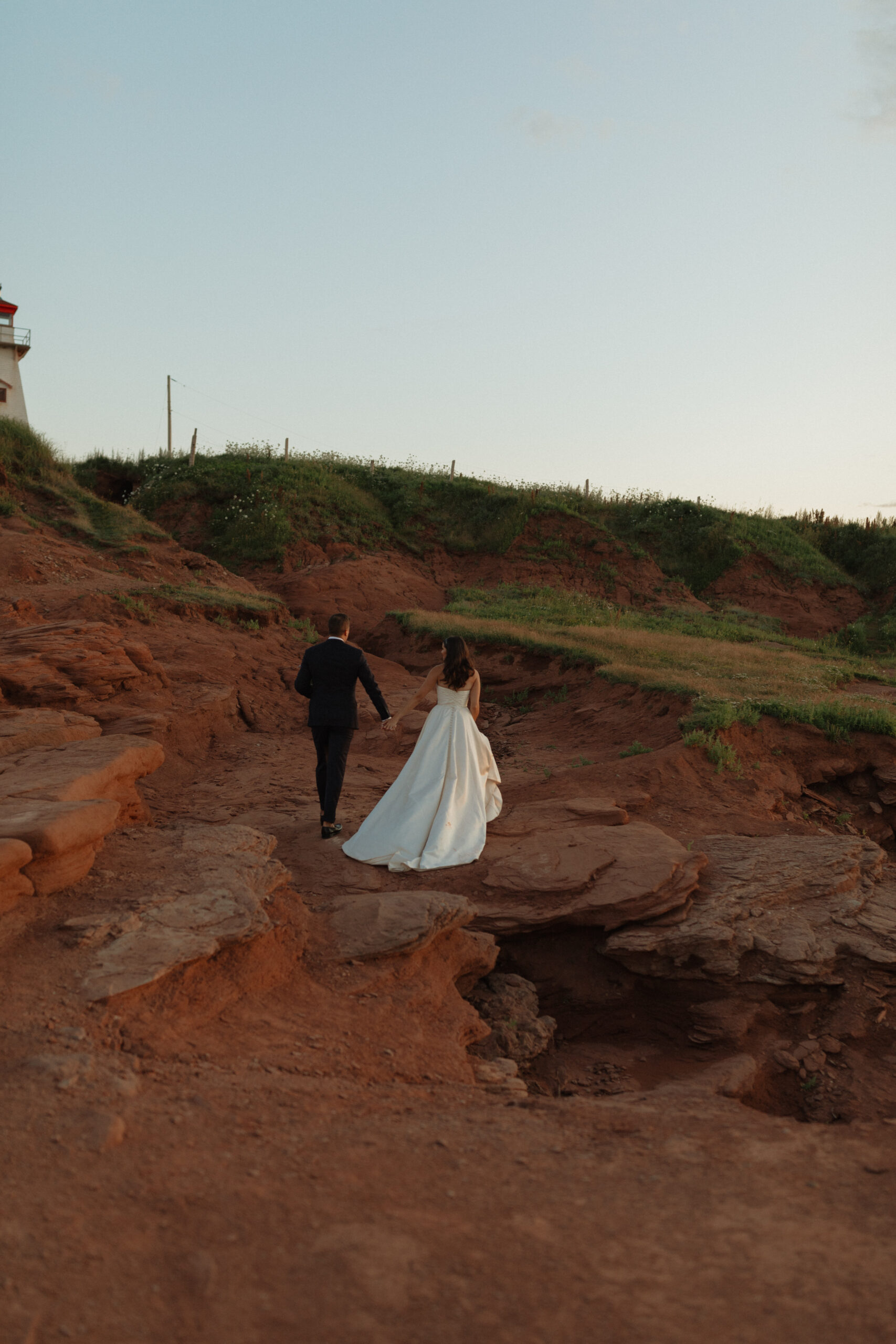 bride and groom holding hand walking on cliffs at sunset