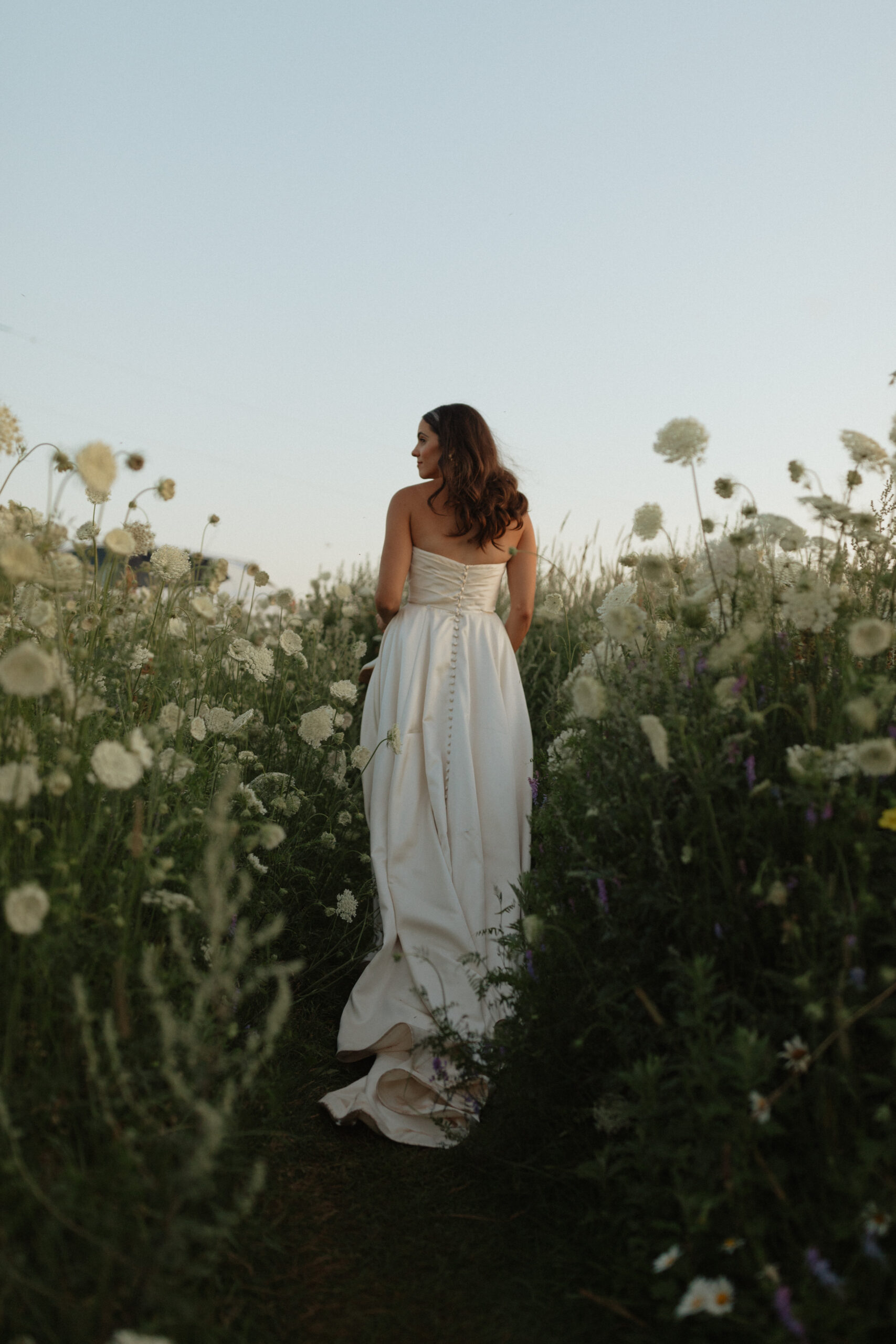 bride walking away from camera through flowers looking to the side