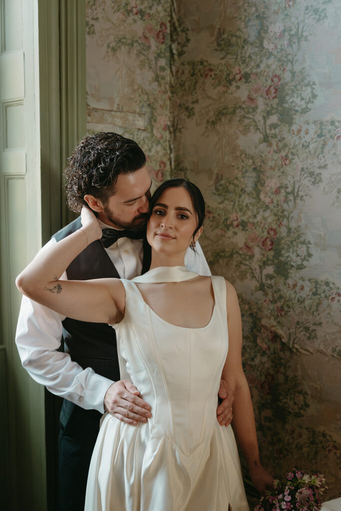 couples portrait of bride and groom, groom is kissing brides head while bride looks at camera