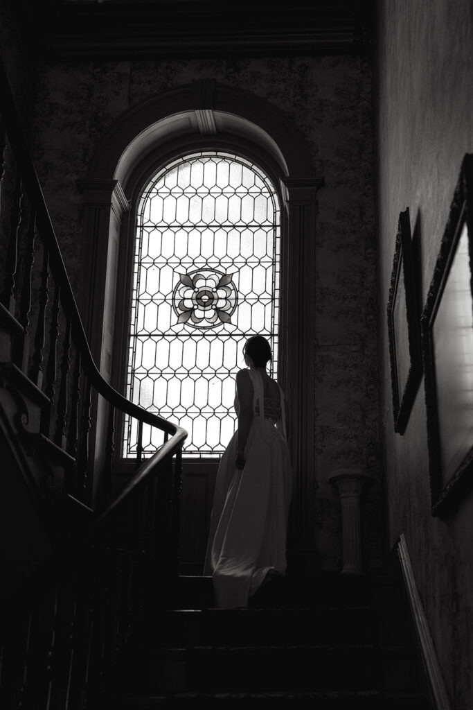 black and white photo of bride looking out vintage arch window inside fairholm inn