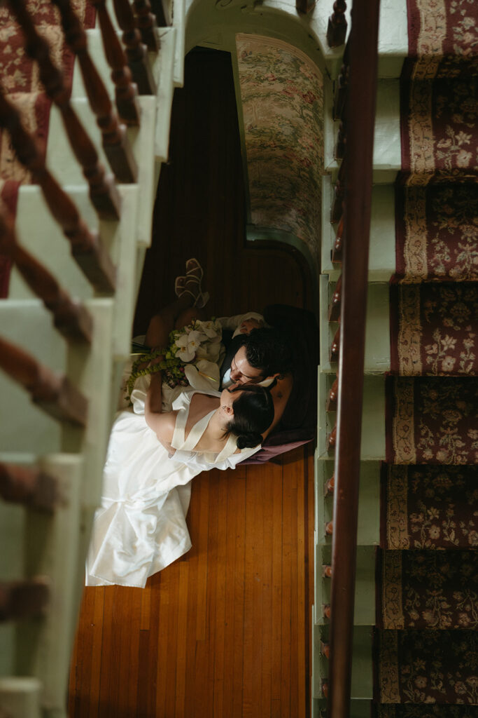 photo looking through the stairs of bride and groom sitting on a chair at the bottom of the stairs