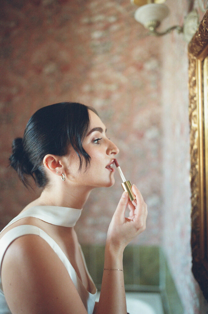 film photo of bride reapplying lip gloss in the mirror during wedding