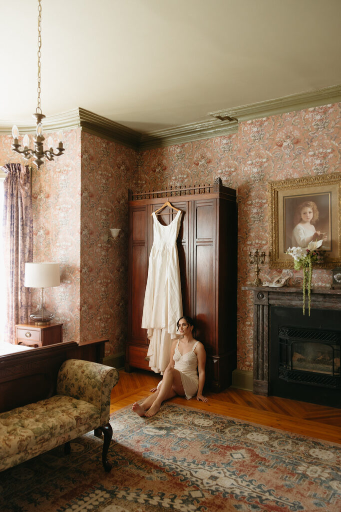bride sitting on floor infront of wedding dress in getting ready room 