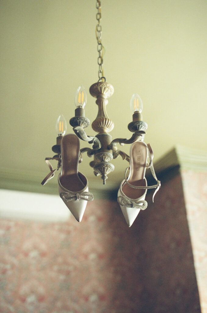 film photo of bride's shoes hanging from chandelier in vintage getting ready suite