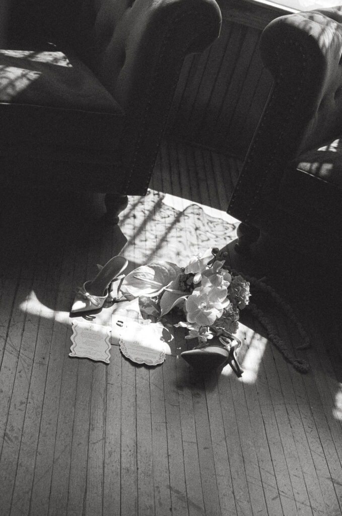 black and white photo of a wedding detail flat lay including invitation suite, shoes, bridal bouquet in the sunlight.