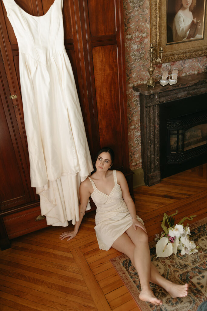 overhead photo of bride looking up at wedding dress while sitting on floor with bridal bouquet