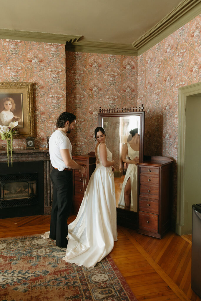 groom helping bride into wedding dress